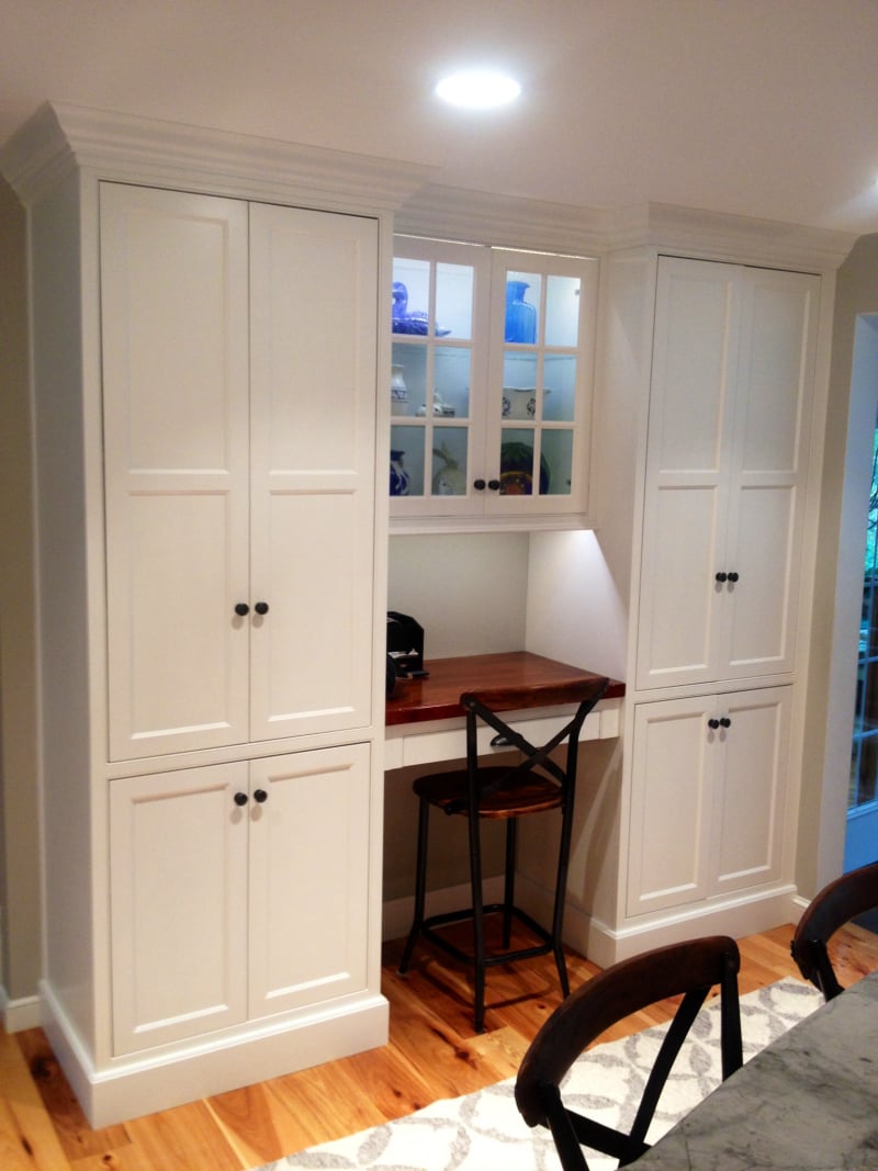 Built-in desk nook flanked by white pantry cabinets, with a leaded-glass cabinet above