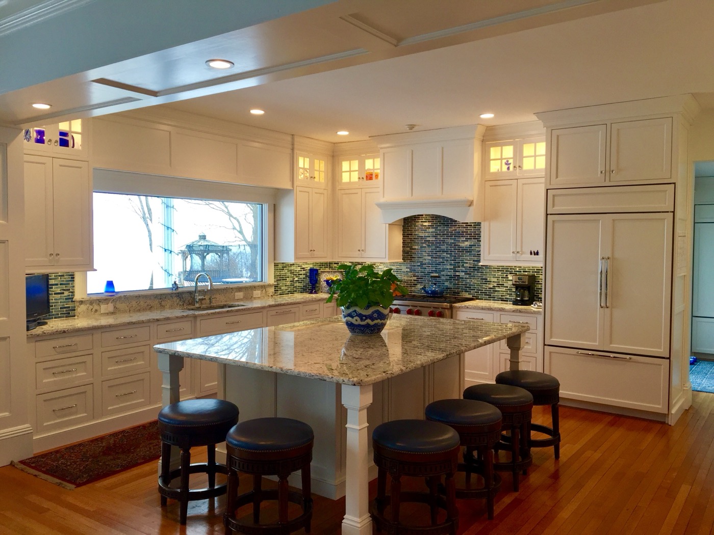 Kitchen with white island, blue glass tile backsplash, and teal chairs